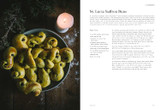Plate of golden saffron buns with raisins, lit candle, wooden surface.