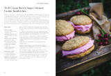 Oatmeal cookie sandwiches with pink filling, on a wooden tray, with berries.