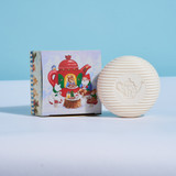Off-white round soap with a teapot stamp, next to its illustrated box showing gnomes.
