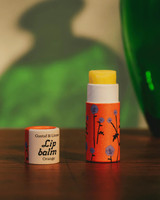 Orange lip balm with blue floral pattern, cap beside it.