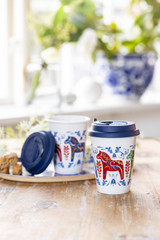 White travel mug with blue Dala horse design and blue lid, on a wooden table.