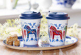 Two white ceramic travel mugs with blue lids and Dala horse designs on a tray.