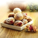 A stack of golden-brown spherical aebleskiver pancakes dusted with powdered sugar and filled with red jam.