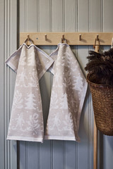 Two beige organic cotton kitchen towels with white Scandinavian holiday patterns, hanging from a wooden rack.
