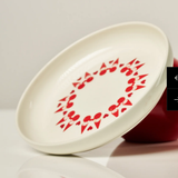 Angled shot of an off-white ceramic Aarikka Tonttu Christmas Elf plate with a red elve pattern.