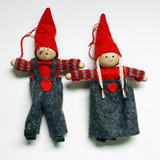 Two felt and yarn Tomte ornaments: boy in overalls, girl in skirt, both with red hats and wooden bodies.