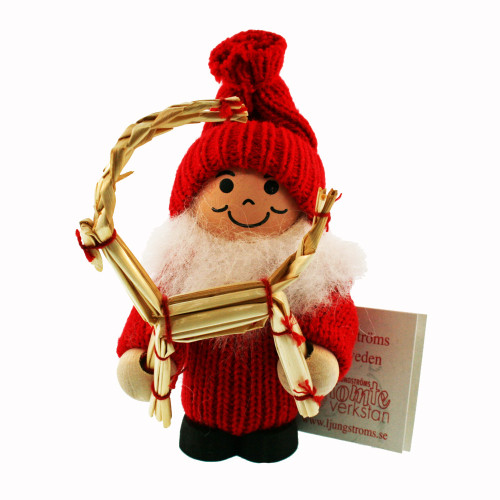 A wooden Santa Tomte doll in a red knitted sweater and hat, holding a woven straw goat ornament.