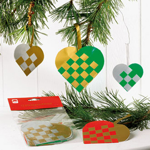 Woven heart ornaments hanging from pine branches. Gold, green, silver, and red paper. DIY kit packaging in foreground.