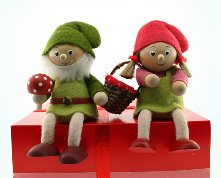 Two wooden elf figurines in green and red clothing sitting on a red box; the male elf holds a mushroom.