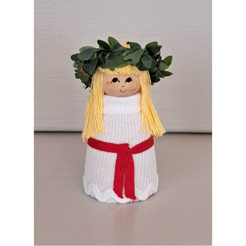 Mini Lucia doll with blonde hair, green leaf crown, white dress, and red sash.