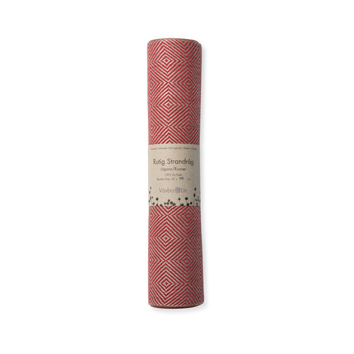 Rolled red linen table runner with a geometric diamond pattern, featuring a Vaxbo Lin paper band.