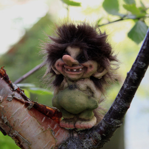 A small, fuzzy troll figurine with a big nose and green belly sits on a tree branch.