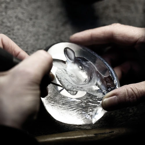 An artisan's hands meticulously engrave a moose motif into a clear cast crystal sculpture.