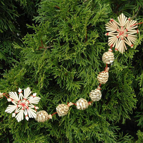 Straw Christmas garland with star and ball ornaments on evergreen branches. Natural straw, red twine.