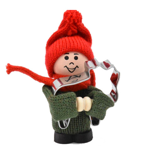 Wooden tomte doll wearing a red hat and scarf, green sweater, and black boots, holding a metal moose cookie cutter.