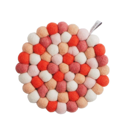 Circular wool ball trivet in shades of coral, pink, orange, and white with a small brand tag.