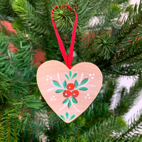 Wooden heart ornament with red lingonberries and green leaves, hanging on a Christmas tree.