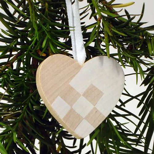 Wooden heart ornament with white woven pattern hanging on a Christmas tree branch.