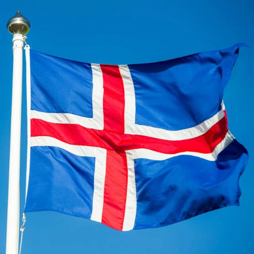 Icelandic flag on a white flagpole, waving against a bright blue sky.