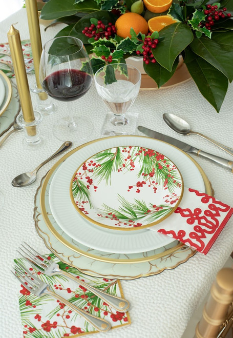 Caspari Berries and Pines paper luncheon napkins feature a red berry and pine needle design, displayed on a holiday table.
