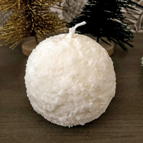 White textured snowball-shaped candle on a dark wooden surface with decorative trees in background.