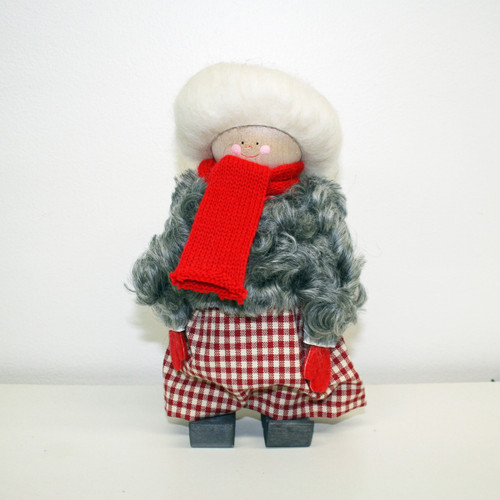 Swallings wooden Jultomtar Mor figurine in a gray sheepskin coat, red scarf, and checkered skirt.