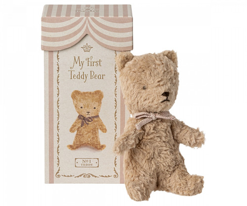 Maileg My First Teddy in powder, featuring a fluffy beige bear with a ribbon, beside its illustrated gift box.