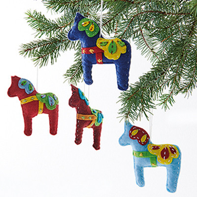 Four felt Dala horse ornaments in red, blue, and burgundy hanging on a Christmas tree.