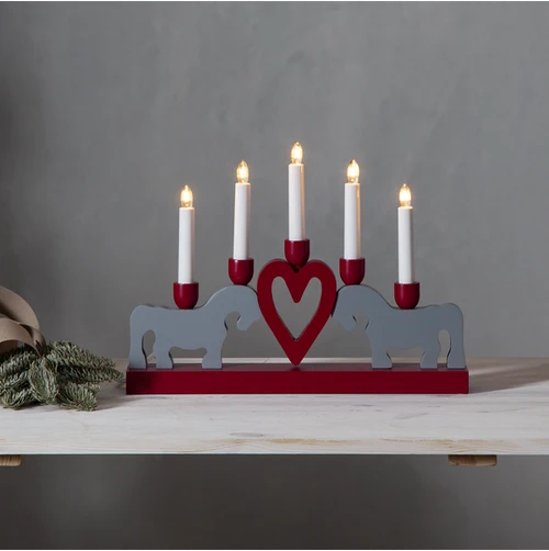 Red-and-grey wooden Leksand candelabra with five lit candles, a central heart motif, and two horse silhouettes on a pale wood