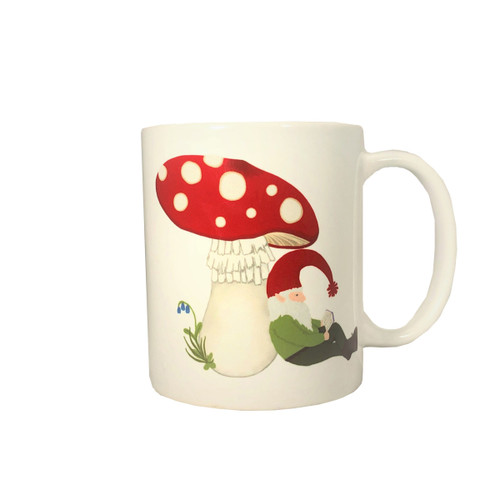 White ceramic coffee mug featuring a gnome reading under a red toadstool mushroom.