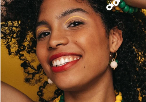 Aarikka Lydia earrings featuring green and white maple beads on gold hoops worn by a woman.