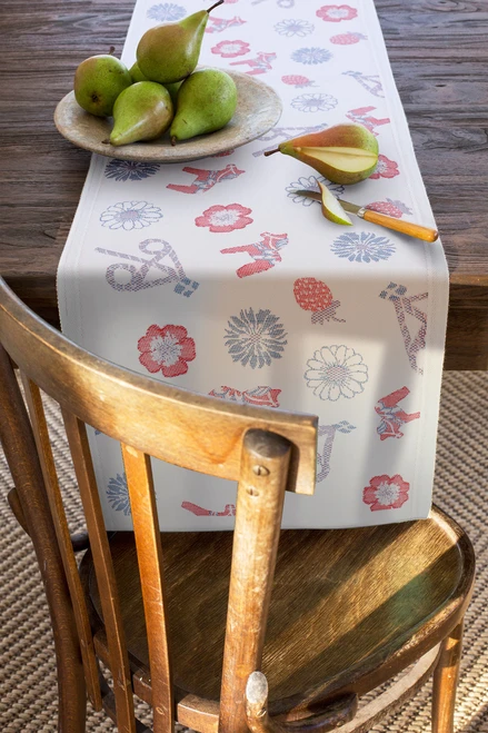 White organic cotton table runner with red and blue Dala horse and flower patterns, on a wooden table.