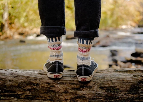 Rear view of person standing on a log wearing Bateau Mouche mismatched crew socks and black sneakers.