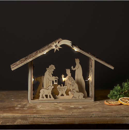 Wooden laser-cut nativity scene with warm LED lights, on a wooden surface.