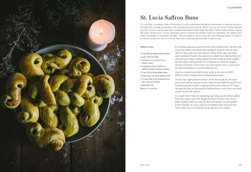 Plate of golden saffron buns with raisins, lit candle, wooden surface.