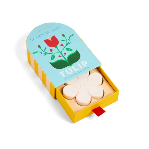 Flower-shaped white soap sliding out of a yellow and blue box with a tulip illustration.