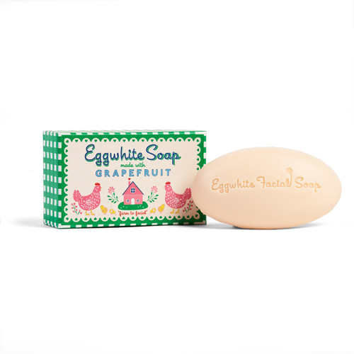 Oval peach-colored facial soap with embossed text, next to its green and white checkered packaging featuring hens.