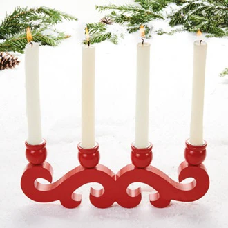 Red wooden Danish candle holder holding four lit candles on snow with pine branches.
