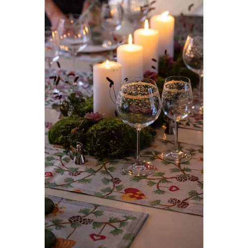 Festive table runner with pinecone and heart pattern, candles, and glassware.