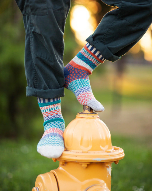 Two mismatched Mirabell crew socks on a yellow fire hydrant; teal, purple, orange, and white patterns.