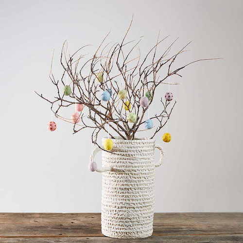 White vase with branches and pastel dotted egg ornaments. Wooden table, neutral background.
