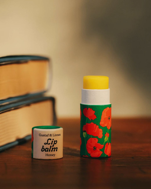 Lip balm tube with poppy design, honey-colored balm extended, green and red, on a wooden surface.