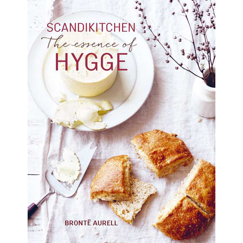Book cover: "SkandiKitchen - The Essence of Hygge". White plate with butter, bread, and a cheese slicer on a linen cloth.