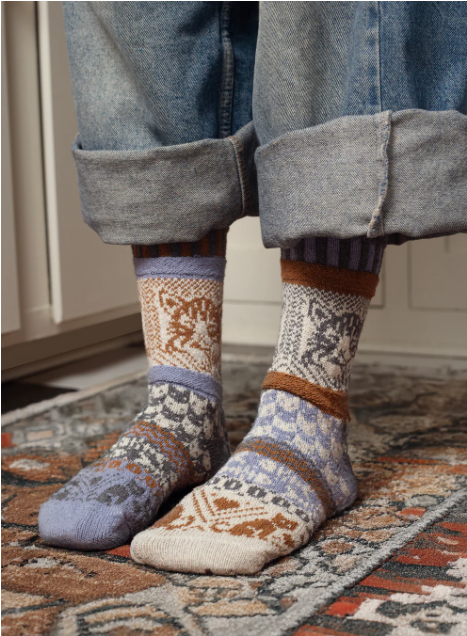 Person wearing blue jeans with cuffed hems and colorful cat-patterned Solmate Socks.