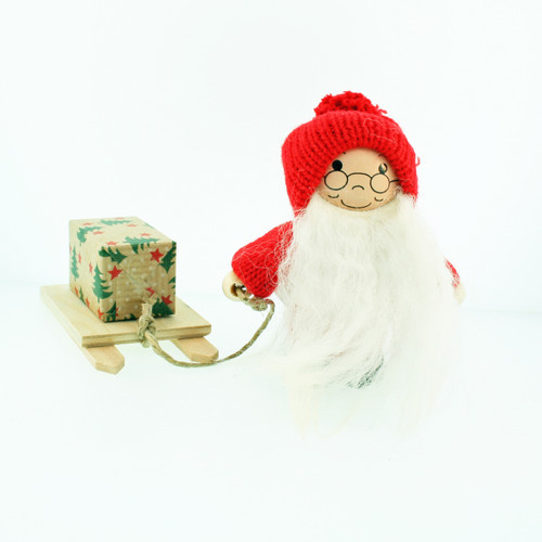 Wooden Tomte Santa figurine wearing a red knit hat and holding a sled with a gift.