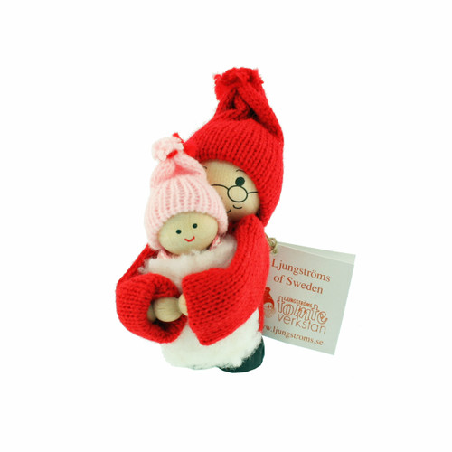 Wooden Swedish Tomte figure in a red suit and hat holding a baby in a pink knit cap.