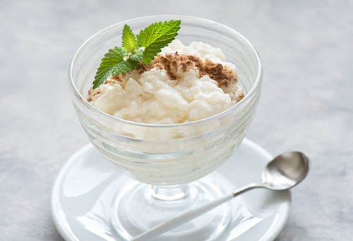Glass dessert bowl filled with creamy rice pudding, topped with cinnamon and mint.