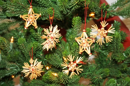 Straw star and snowflake ornaments hanging on a Christmas tree; natural straw, red string.