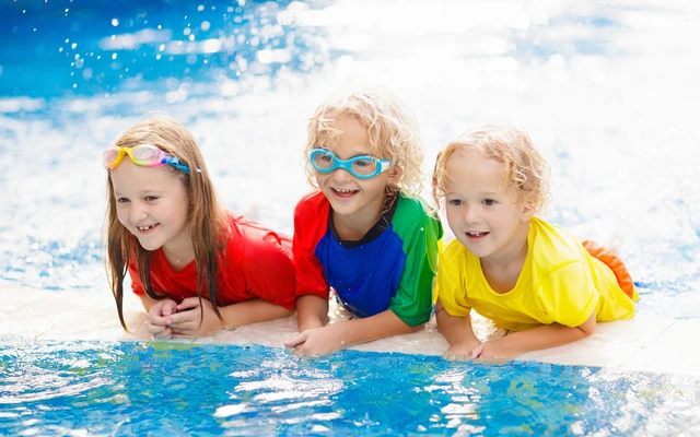 three young girls kicking water in a swimming pool