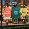 Three storefront window clings advertising a grand opening, winter sale, and local market event.